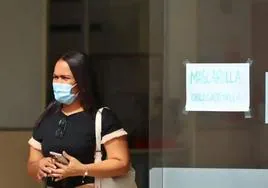 Una mujer sale con mascarilla de la entrada de urgencias, con el cartel que indica la obligatoriedad de la protección