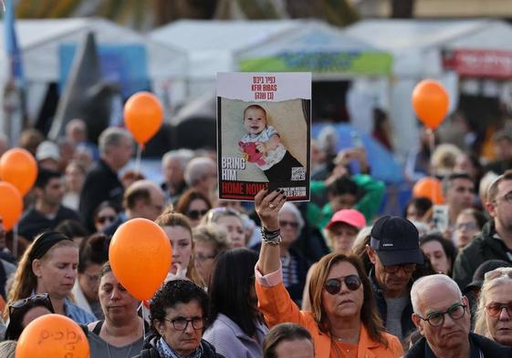 Un asistente a un acto por el cumpleaños de Kfir sostiene las fotos del pequeño, su hermanos y sus padres, secuestrados por Hamás.