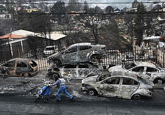 Una mujer con su bebé pasa junto a vehículos quemados por los incendios forestales en la ciudad chilena de Viña del Mar.