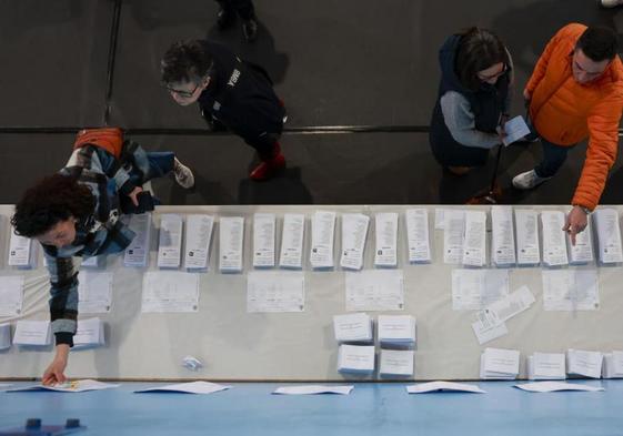 Varias personas escogen papeletas para ejercer su derecho al voto en el pabellón polideportivo Ames en A Coruña durante la jornada electoral en Galicia, este domingo. Los colegios electoral.
