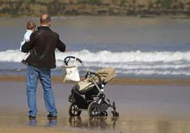 Un padre con permiso de paternidad pasea con su bebé en la playa.