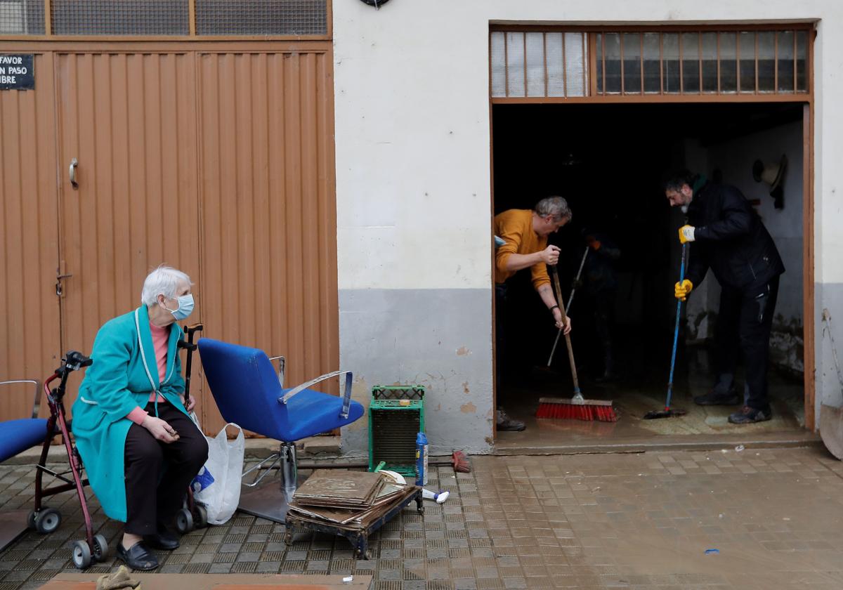 Una mujer observa a dos voluntarios achicando agua de su casa tras las inundaciones registradas en Villava, Navarra.