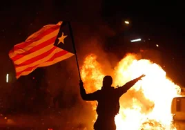 Un manifestante ondea una bandera independentista catalana junto a contenedores de basura ardiendo durante una protesta convocada por el movimiento separatista catalán Tsunami Democrático
