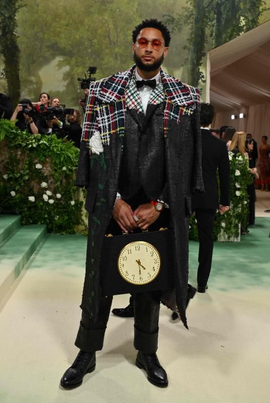 El jugador de baloncesto Ben Simmon, de los Brooklyn Nets de la NBA, con un abrigo oversize de hombros cuadrados de Thom Browne en tweed de algodón de tartán multicolor sobre una chaqueta y pantalones en tweed, todo deshilachado y pintado a mano en negro con rosas blancas bordadas.