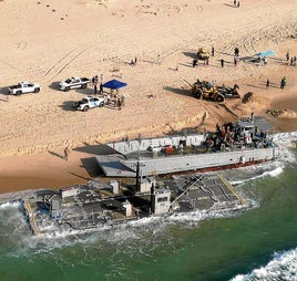 Parte de la estructura del muelle flotante y un buque, embarrancados en una playa israelí.