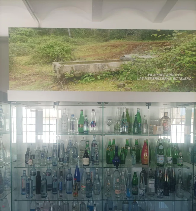 Una vitrina llena de botellas de agua bajo un panel con uno de los manantiales del pueblo.