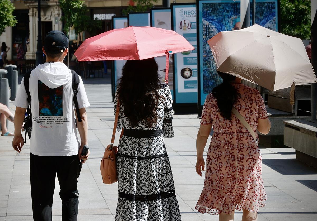 Varios turistas se cubren del sol con sombrillas mientras pasena este martes por Sevilla.