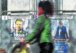 Una mujer camina junto a los carteles de los candidatos presidenciales franceses Macron y Le Pen en las elecciones de 2022.