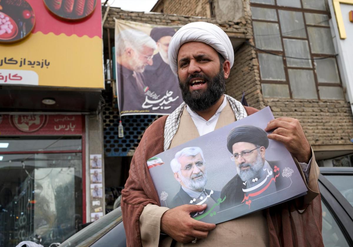 Un clérigo muestra un cartel favorable a Saeed Jalili, que aparece junto a la imagen del expresidente Ebrahim Raisi.