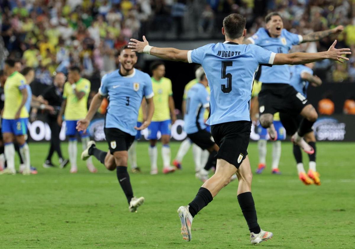 Los futbolistas uruguayos celebran la victoria en los penaltis con los brasileños de fondo.