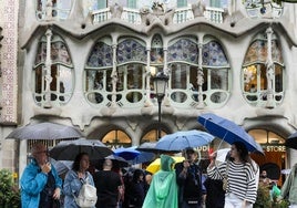 Varios turistas se protegen de la lluvia en las inmediaciones de la Casa Batlló del paseo de Gracia de Barcelona.