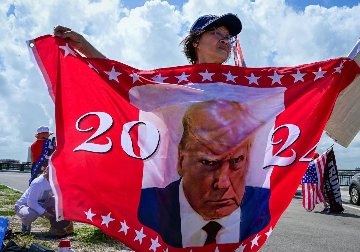 Una mujer porta una bandera con la icónica imagen de Trump en su ficha policial.