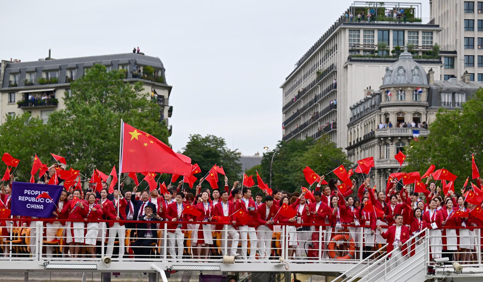 La delegación olímpica de la República Popular China ondea banderas mientras navega en su barco por el río Sena.