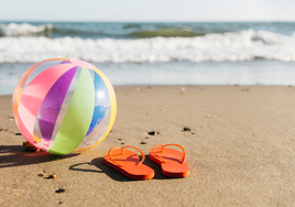 Pelota hinchable en arena mojada de playa con chanclas naranjas al lado.