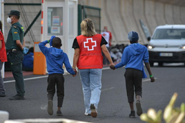 Un efectivo de la Cruz Roja escolta a dos de los menores que viajaban con otros 313 inmigrantes y que han sido trasladados desde El Hierro a Tenerife