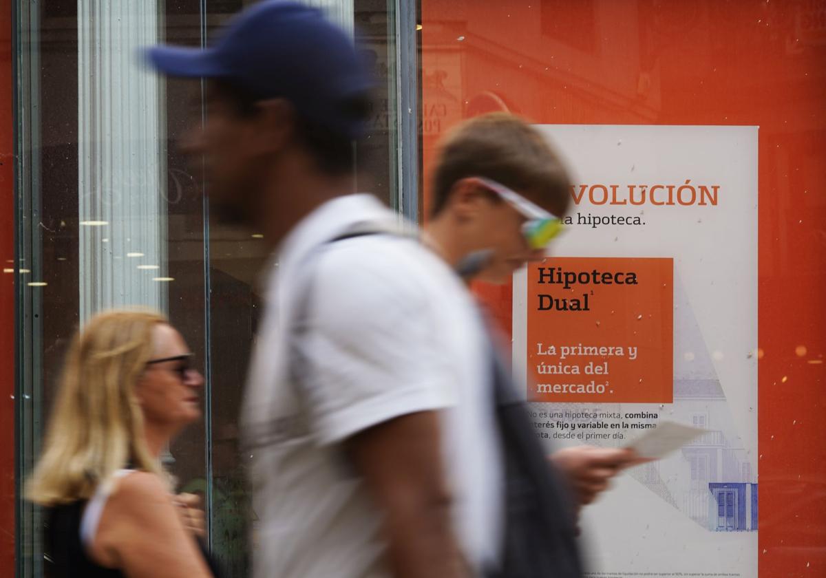 Unas personas caminan frente al escaparate de una sucursal bancaria.