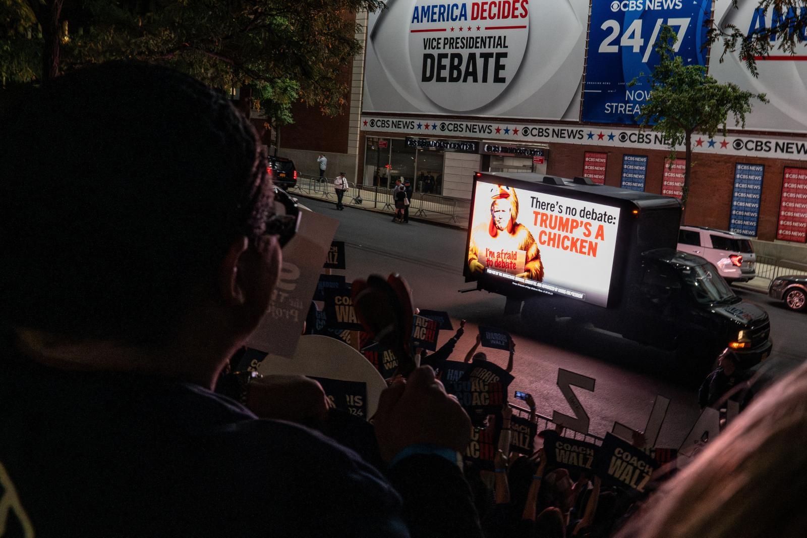 Ambiente en el exterior de los estudios de la CBS en Nueva York, con periodistas, curiosos y una crítica incluida a Trump en un camión.