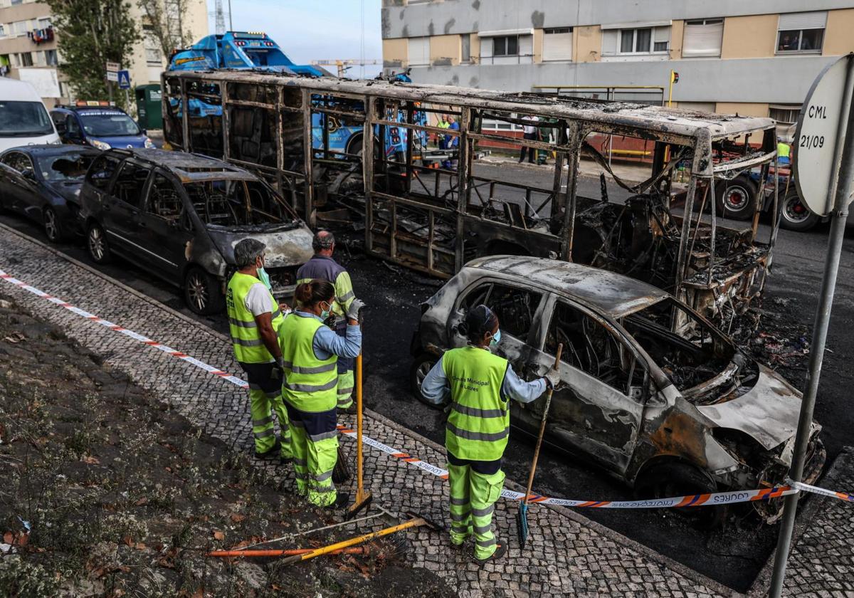 Operarios de limpieza observan los restos de un autobús y varios vehículos calcinados por los altercados en la capital portuguesa.