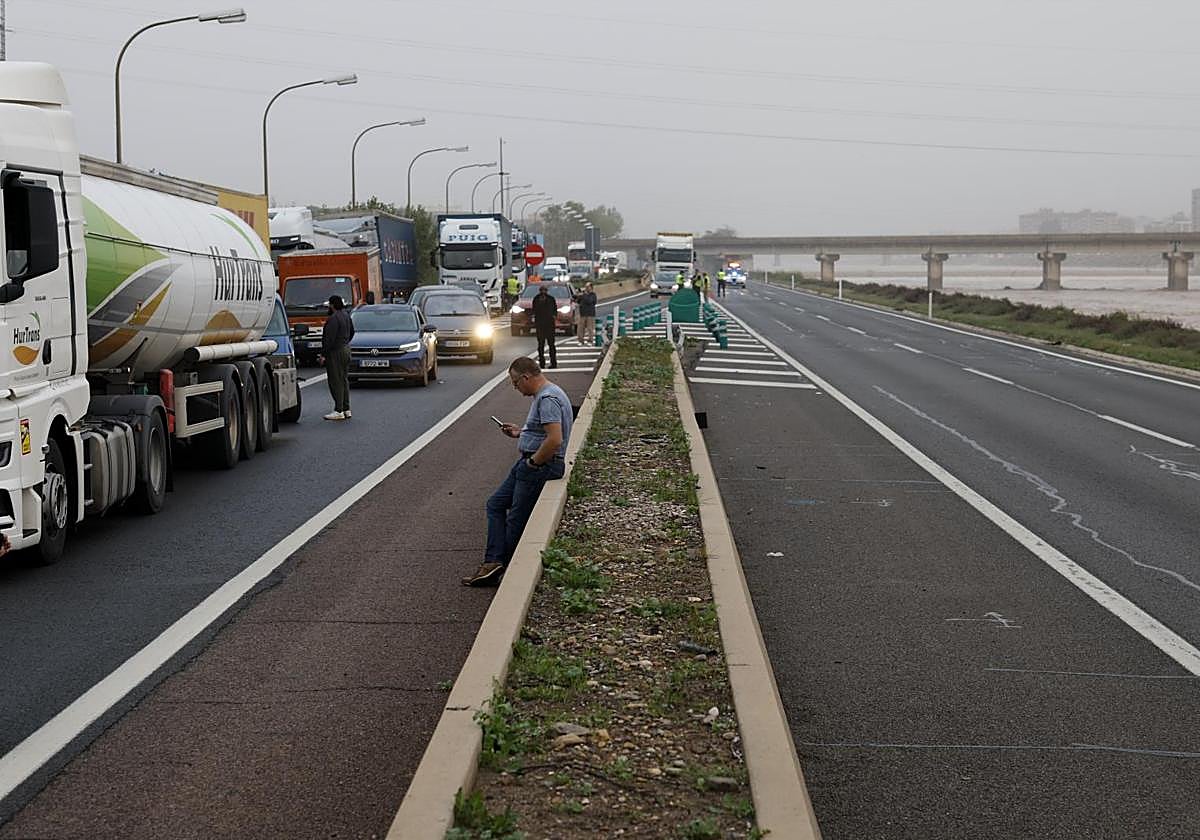 Varios conductores aguardan junto a sus vehículos en la V-30 junto al nuevo cauce del Turia.