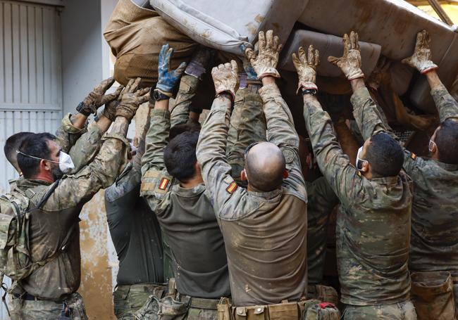 Varios militares sostienen un sofá destrozado por el agua