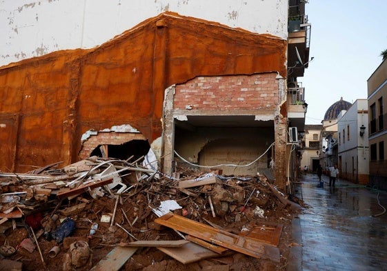 Una persona ayuda a limpiar una calle cerca de un montón de escombros y barro en Paiporta