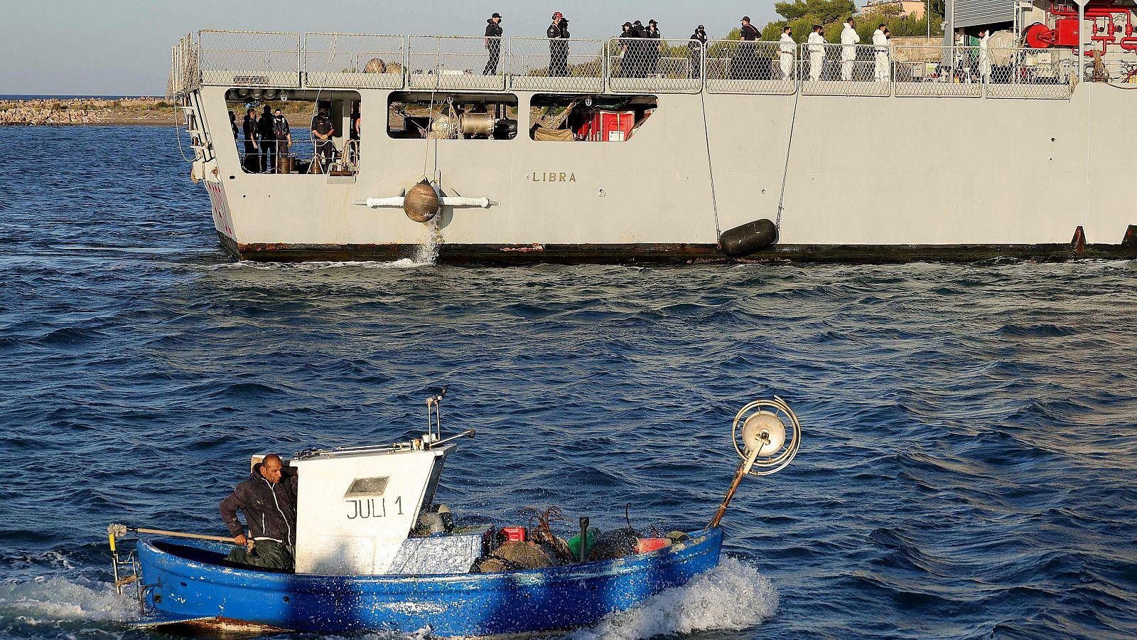 Una barca pesquera navega junto al 'Libra', el buque militar que transporta a los migrantes.