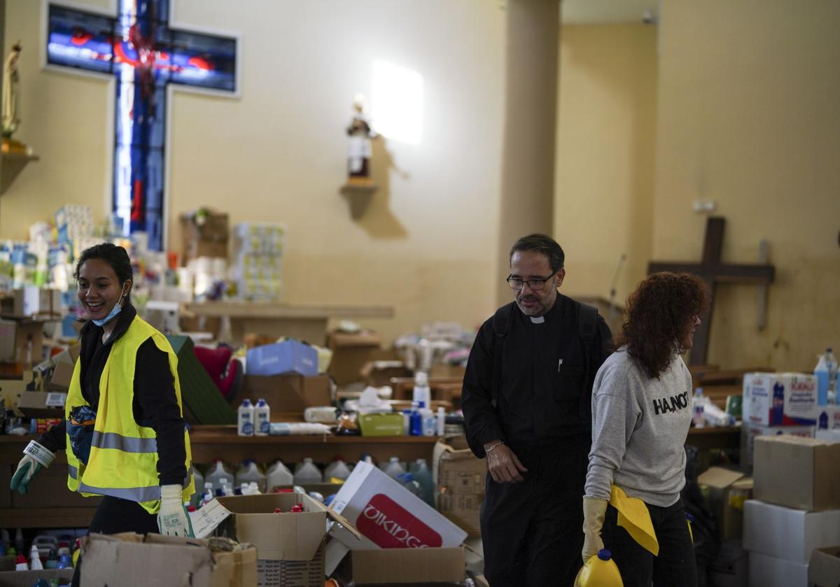 Imagen principal - El cura de San Ramón, en la iglesia reconvertida en un centro logístico de reparto de ayuda; Un detalle del corporal completamente blanco cubriendo el cáliz, tal y como se lo encontró el párroco en la sacristía inundada de barro; Aspecto de la sacristía al día siguiente de la DANA con la imagen del corporal y el cáliz encima de una mesita.