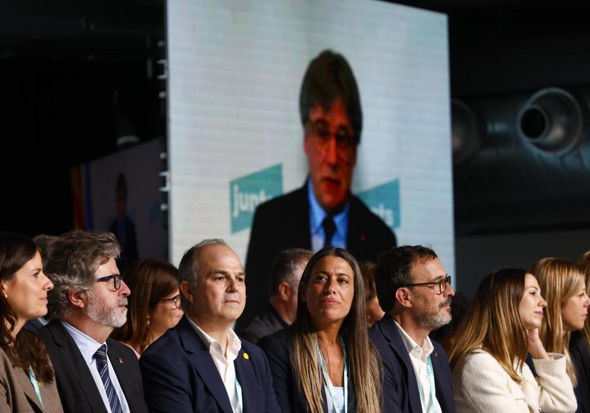 El secretario general de Junts, Jordi Turull (c), escucha la intervención de Carles Puigdemont (en las pantallas) durante el Congreso del partido en octubre