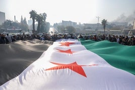 Los ciudadanos despliegan una enorme bandera rebelde en Damasco un día después de la conquista.