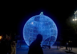 Varias personas junto a una bola navideña iluminada, en Plaza de España, en Madrid.