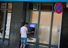 Hombre saca dinero de un cajero automático del Banco Sabadell.