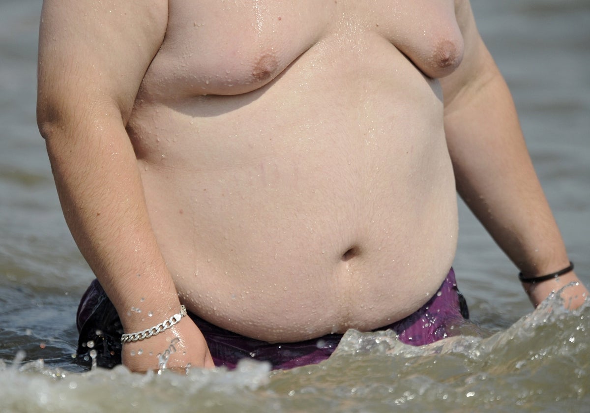 Un hombre obeso sale del mar en una playa española.