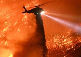 Un helicóptero de extinción arroja agua a un monte en llamas.