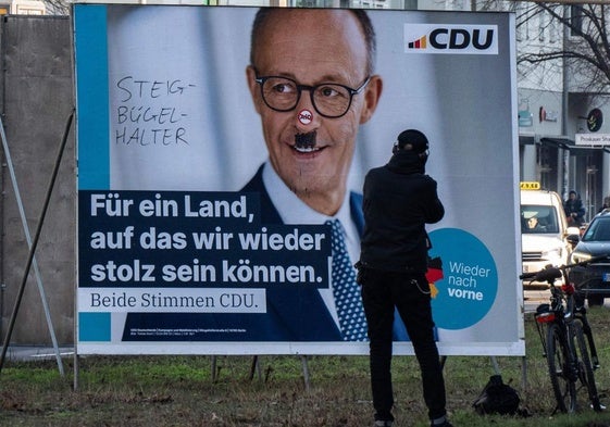 Un hombre toma una fotografía de un cartel de campaña electoral desfigurado del candidato de la Unión Demócrata Cristiana (CDU), Friedrich Merz, en Berlín.