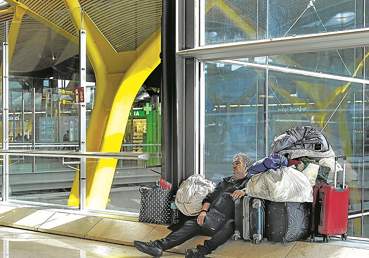 Un hombre sin hogar descansa junto a sus pertenencias en la T4 de Barajas.