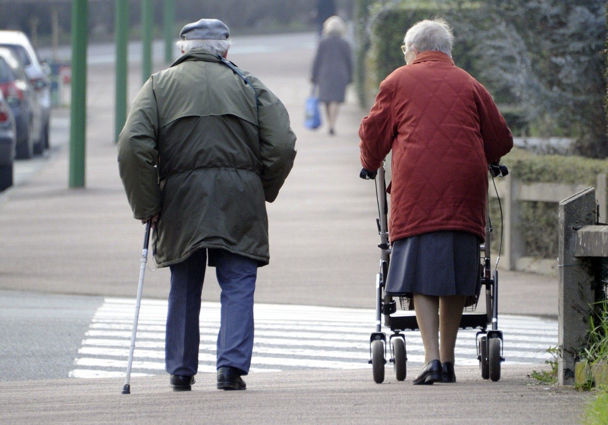 Una pareja de ancianos con problemas de movilidad caminan por la calle.