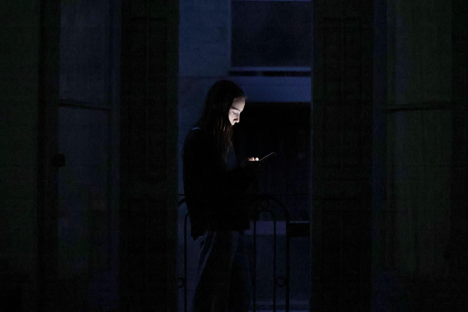 Una joven a oscuras mira la pantalla de su teléfono