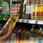 Un consumidor coge una botella de aceite de oliva en un supermercado.