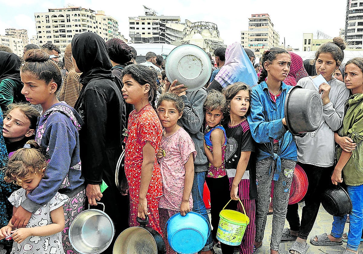 NIños y adultos hacen cola para conseguir algo de comida en Gaza.