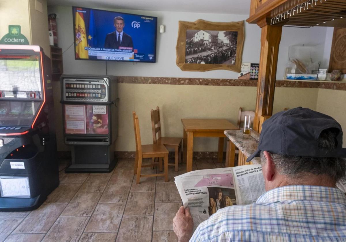 Un vecino de la zona ojea el perfil de Leire Díez en el periódico mientras Núñez Feijóo denuncia el caso en televisión.