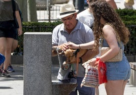 Un hombre y una joven remojan a su mascota en una fuente de Sevilla el pasado viernes, cuando se alcanzaron los 40 grados en la capital hispalense.