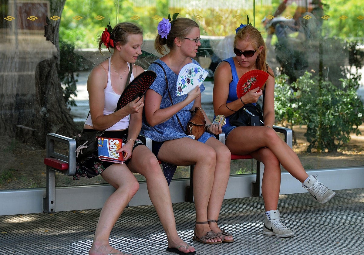 Three tourists try to alleviate the high temperature by fanning themselves on a bench in the shade.