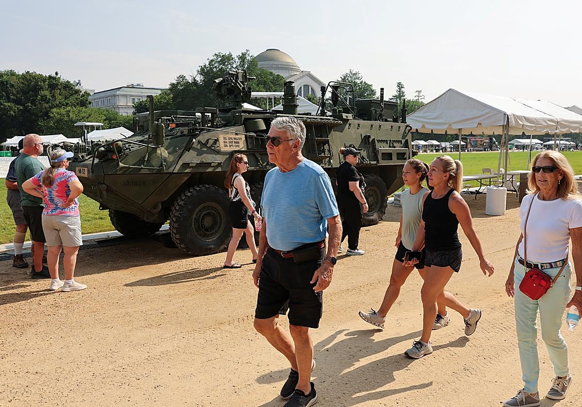 Ciudadanos pasean junto a un vehículo aparcado a la espera del desfile militar.