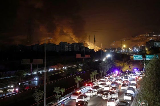 La Policía dirige a los coches hacia una salida de la capital con unos depósitos de combustible ardiendo al fondo.