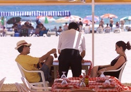 Un camarero atiende a dos clientes en un chiringuito de la playa de San Juan (Alicante)