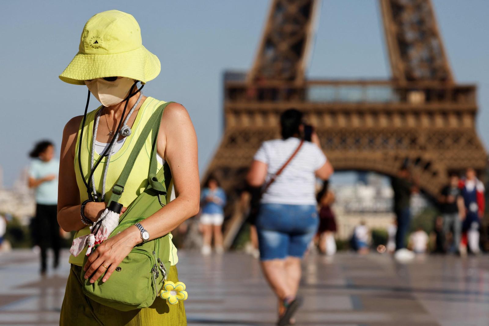Una joven camina bajo el calor y protegida contra la contaminación al lado de la Torre Eiffel.