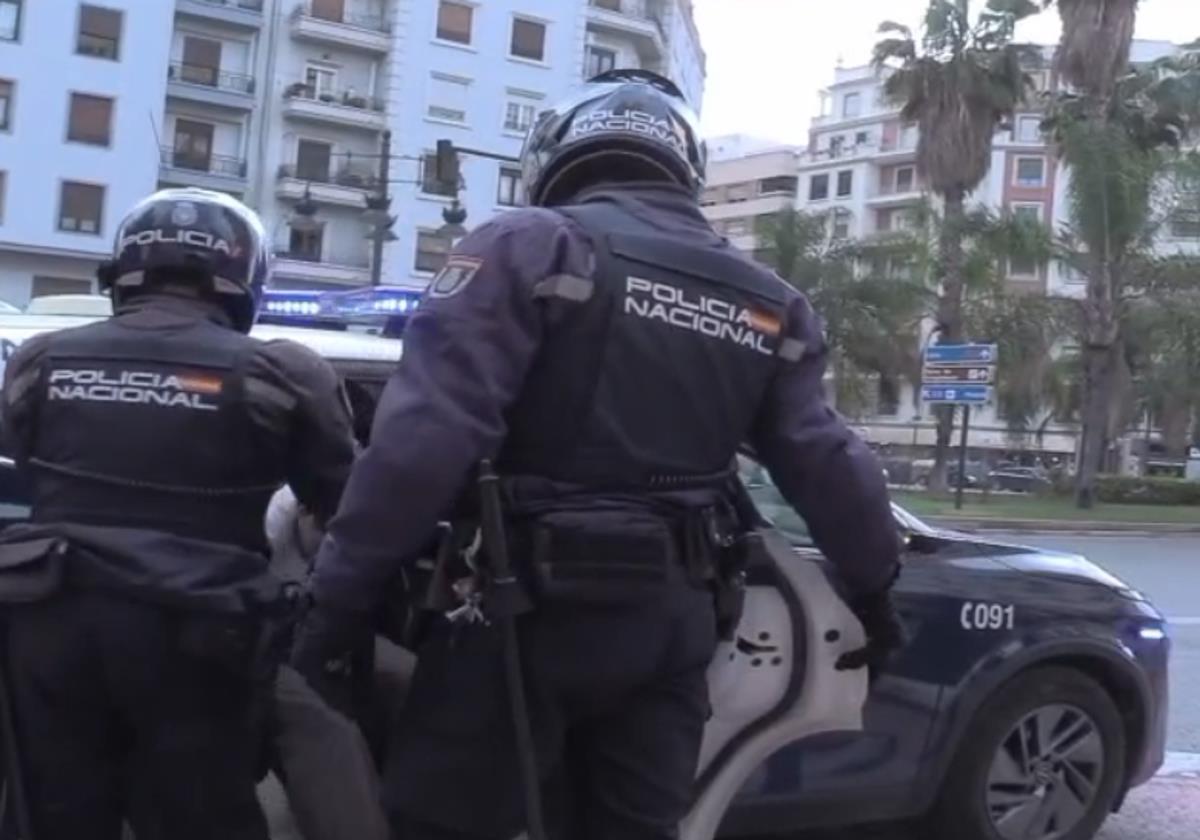 Dos policías sacan al violador del portal de un coche patrulla.