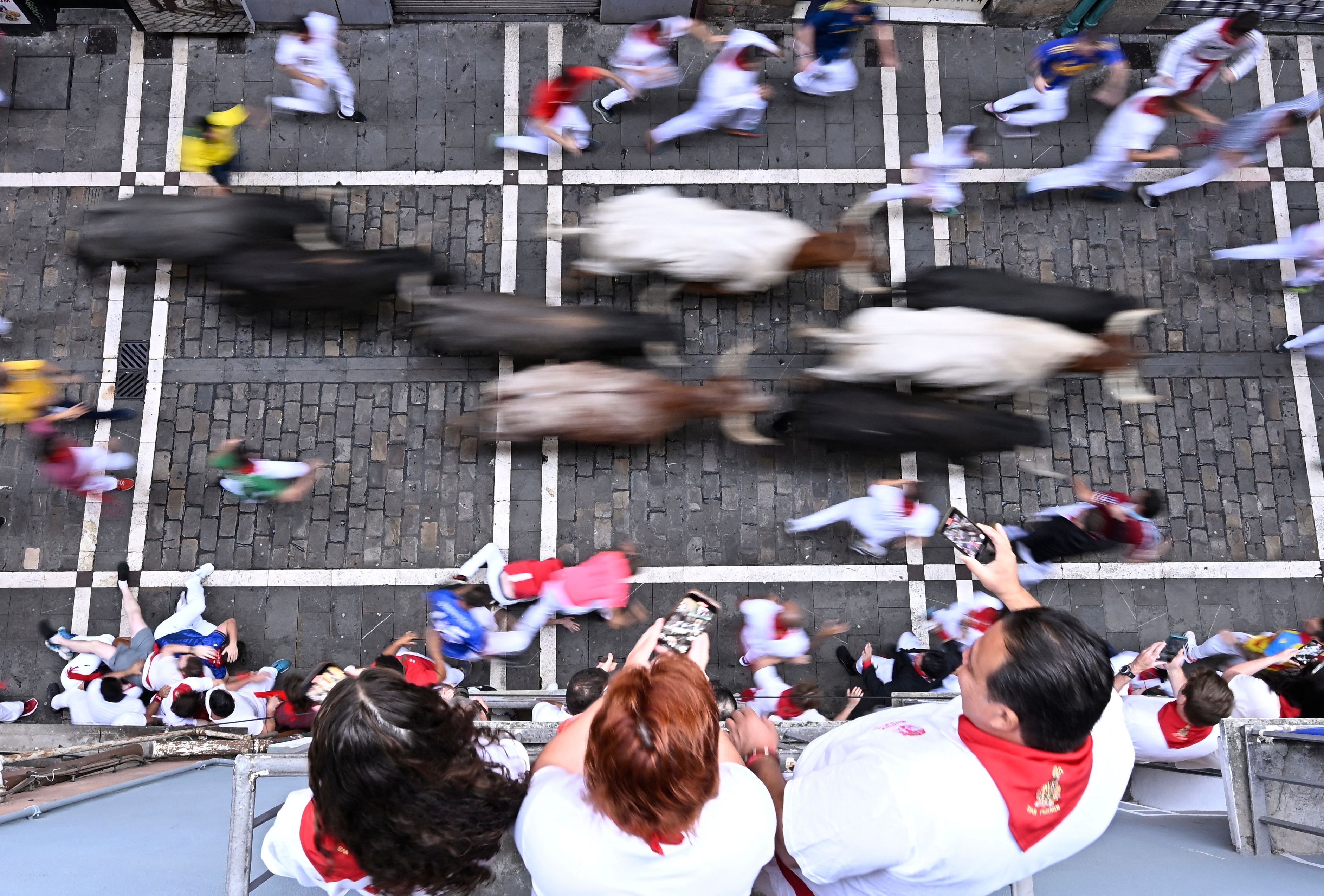 Varias personas miran los toros pasar desde las terrazas en Pamplona.