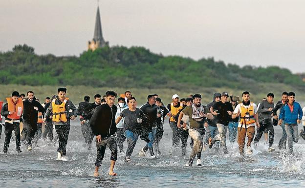 Migrantes corren desde la playa hacia el agua para alcanzar un bote en el que cruzar el canal.