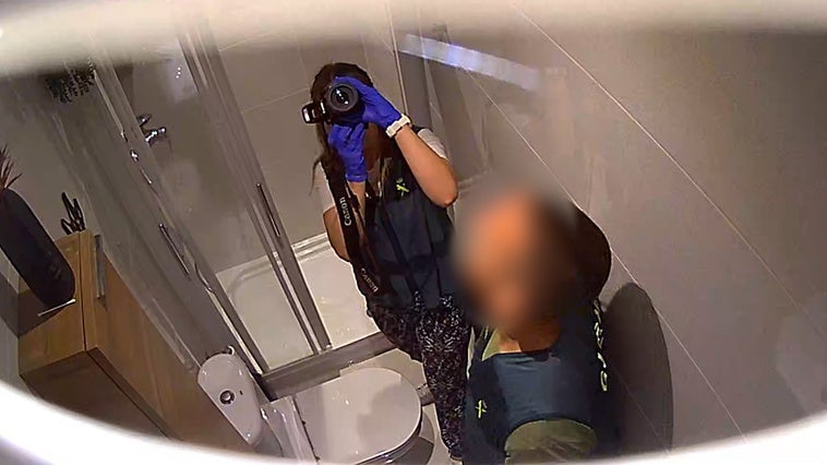Punto de vista de la cámara oculta muestra agentes de la Guardia Civil investigando el baño.